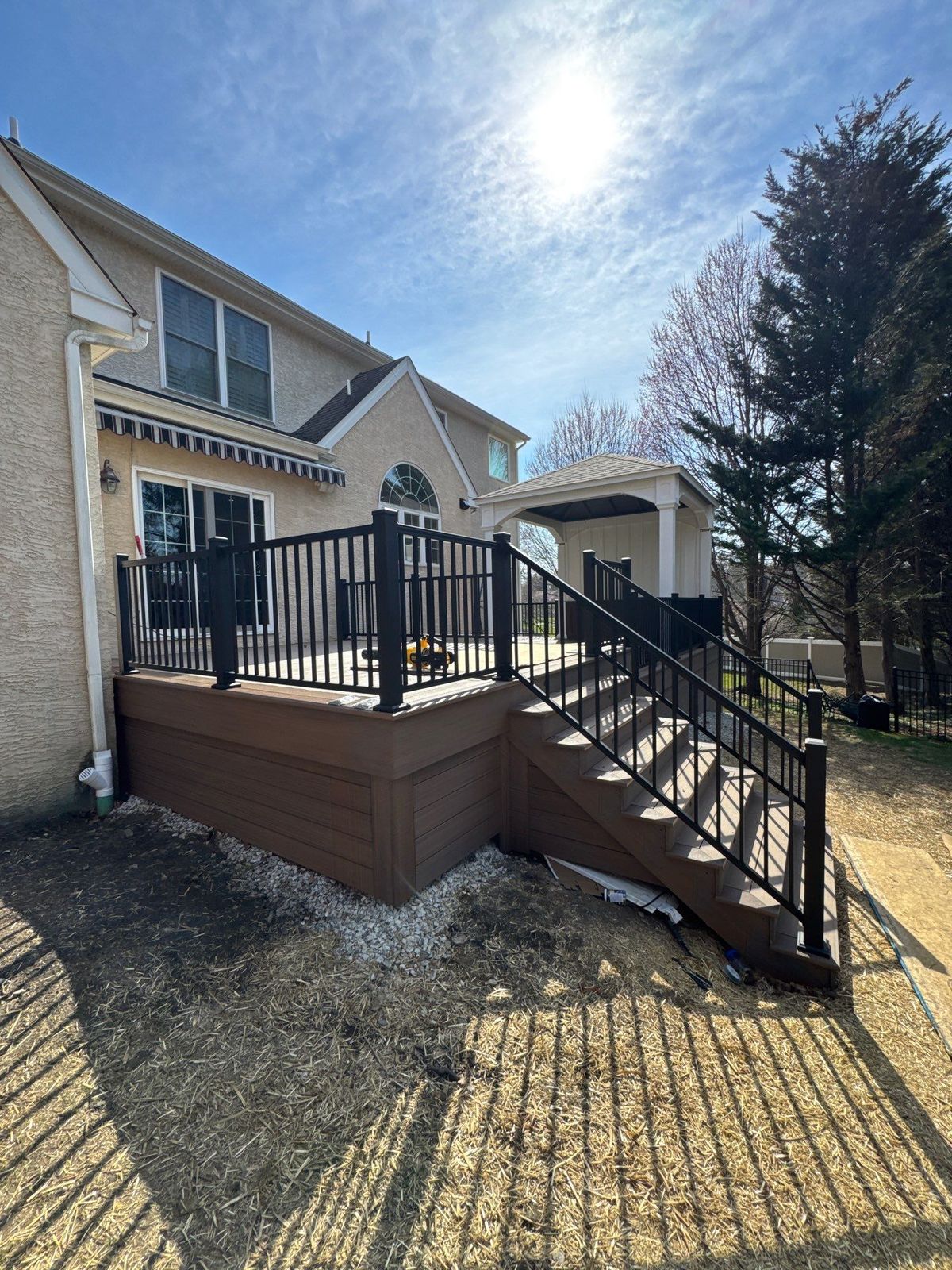 Raised brown composite second-story deck with black aluminum railing and stairs on a stucco home in Chester County, PA