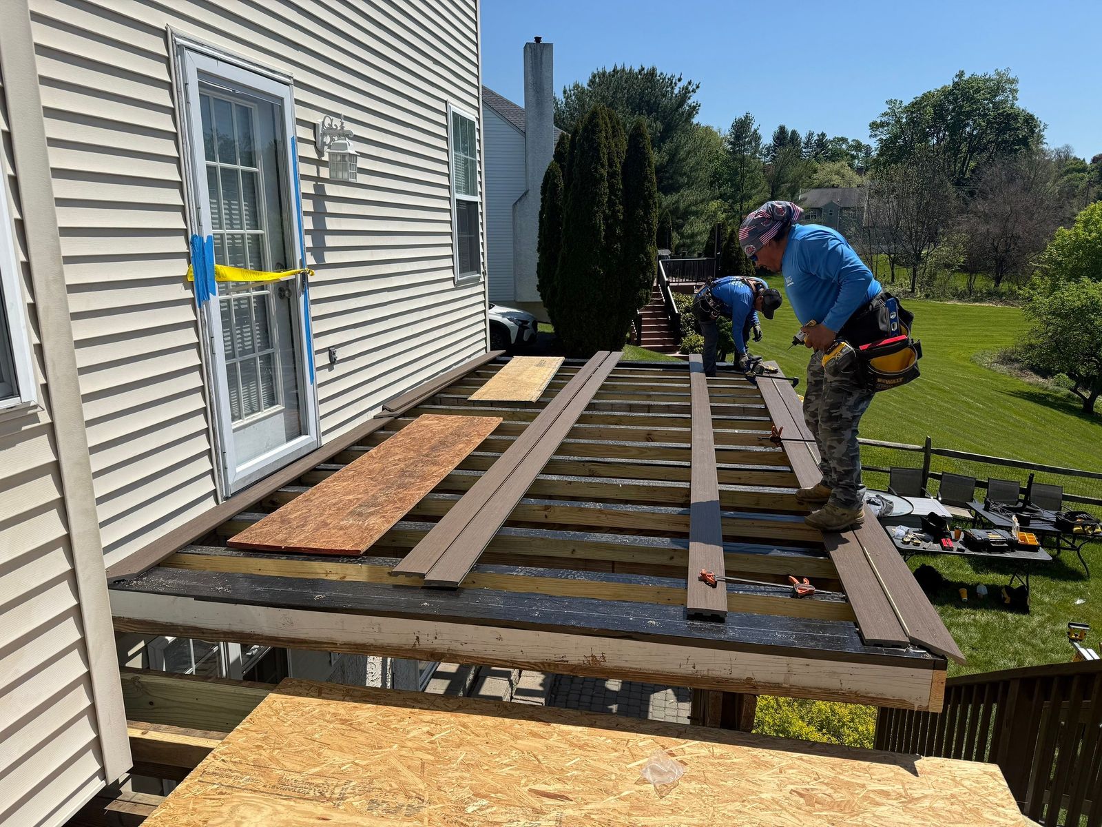 JHL crew installing brown composite deck boards over framing on an elevated backyard deck in suburban Delaware County PA