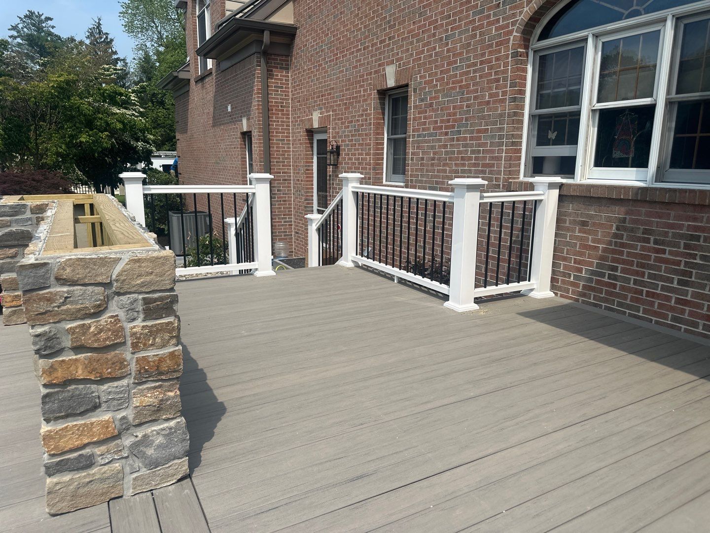 Gray composite deck with white posts, black aluminum railing and a stone seat wall at a Main Line PA brick home
