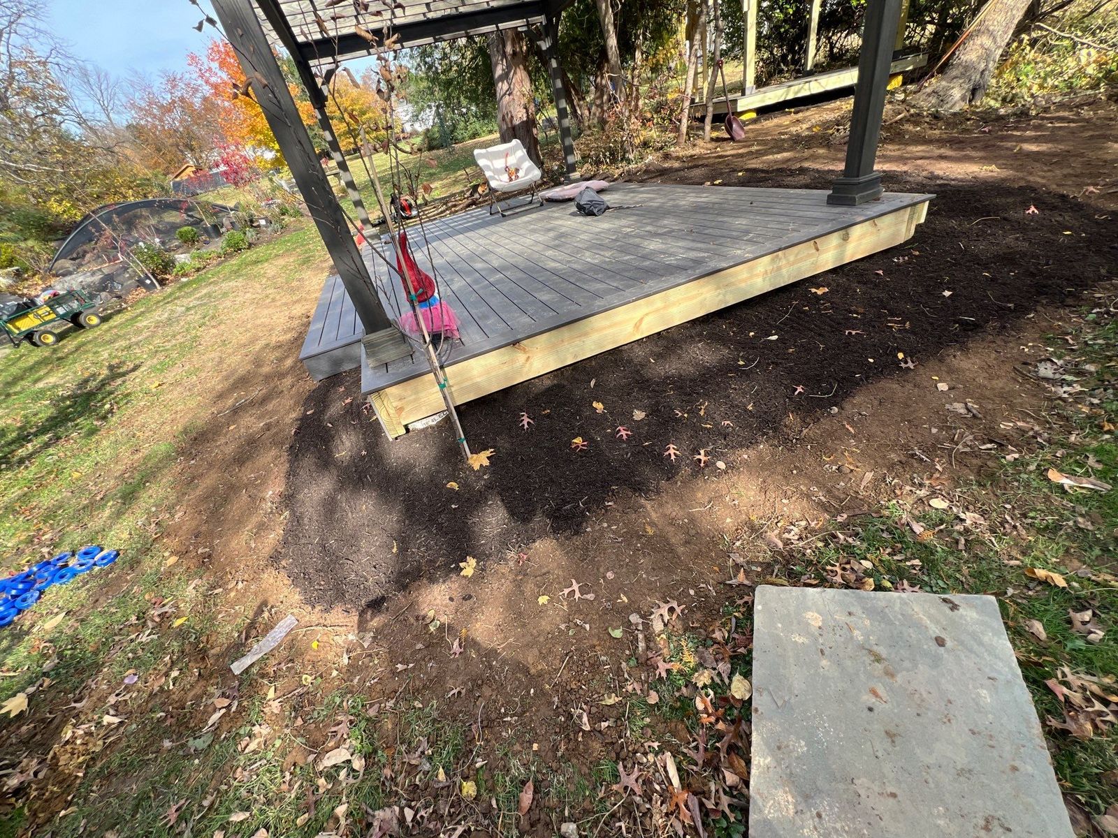 Low gray composite deck platform beneath a wood pergola in a wooded Chester County PA backyard
