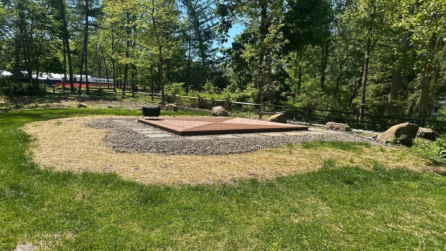Low ground-level wood deck platform beside a fire pit in a wooded backyard near Newtown Square, PA