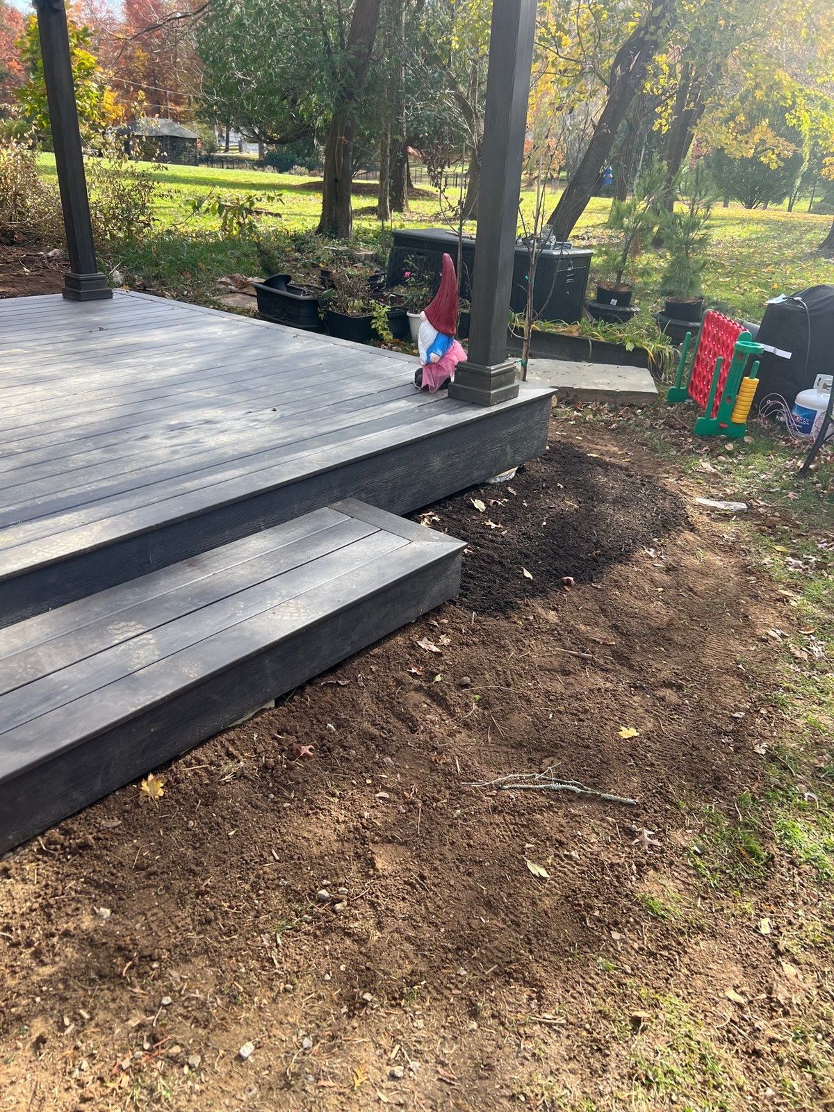 Low gray composite deck with a single step and fresh grading in a wooded Chester County PA backyard