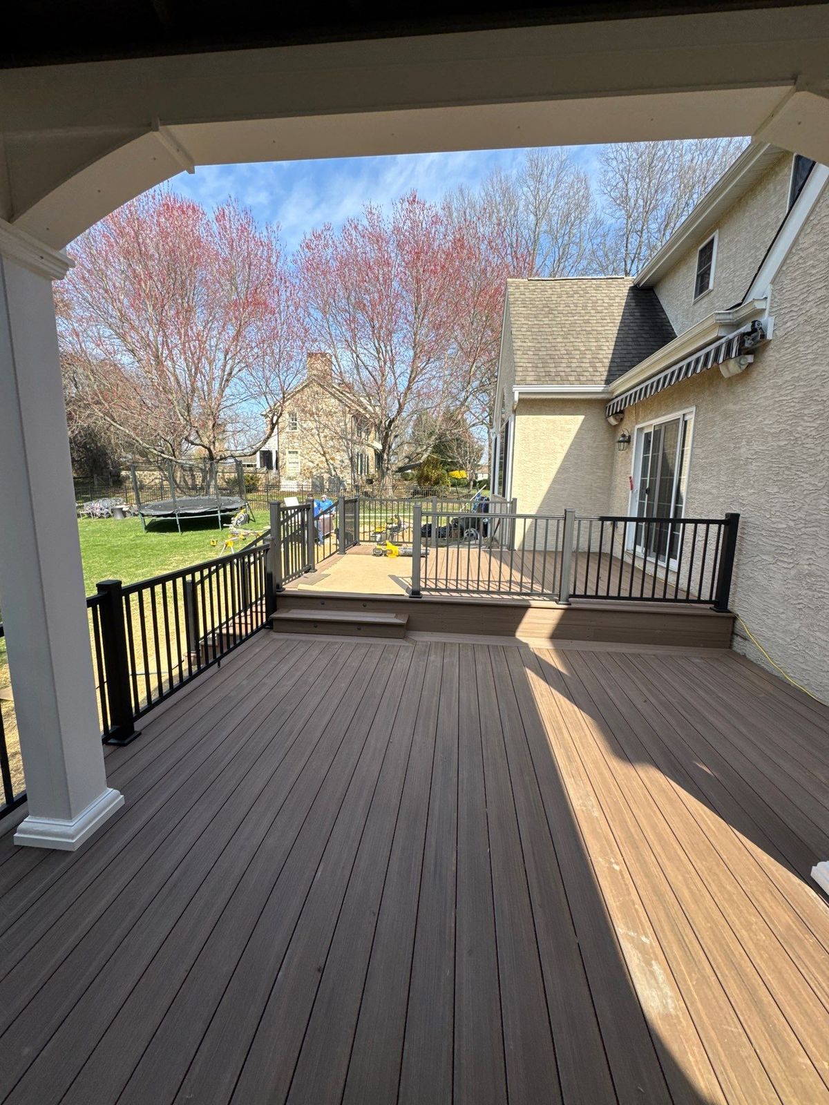 Multi-level brown composite deck with covered porch and aluminum railing at a stucco Main Line PA home