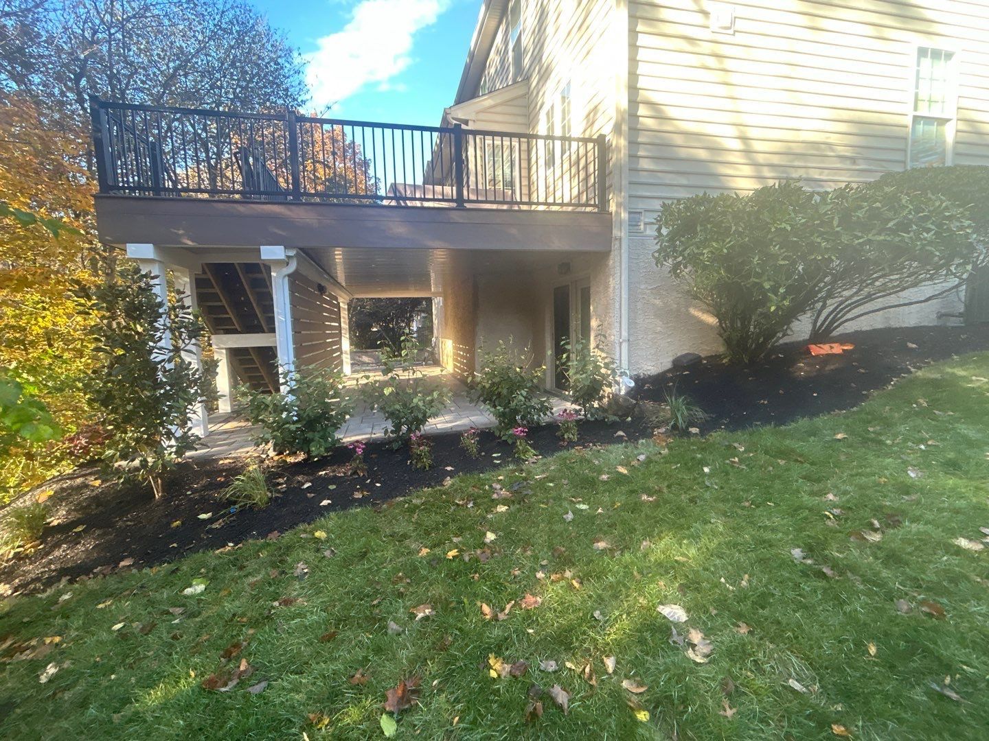 Elevated second-story composite deck with black railing and white columns over a paver patio at a Newtown Square PA home