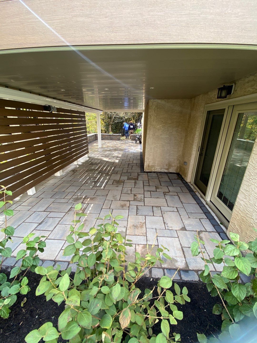 Paver patio beneath a covered second-story deck with privacy screening at a stucco Main Line PA home