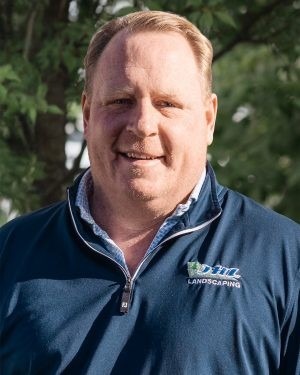 TJ Warner, owner of JHL Deck Builders, outdoors in a navy JHL pullover